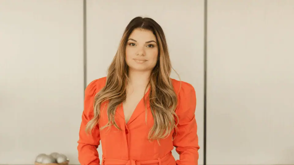 Dra. Camila Chagas em pé no escritório, de conjunto laranja